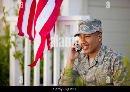 Lächelnden jungen Armee Soldaten im Gespräch mit einem Mobiltelefon außerhalb seines Hauses. Stockfoto