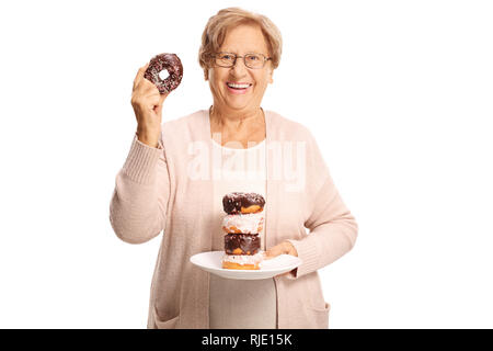 Freundliche ältere Frau, die eine Platte von Donuts in der einen Hand und einem Donut in der anderen Hand auf weißem Hintergrund Stockfoto
