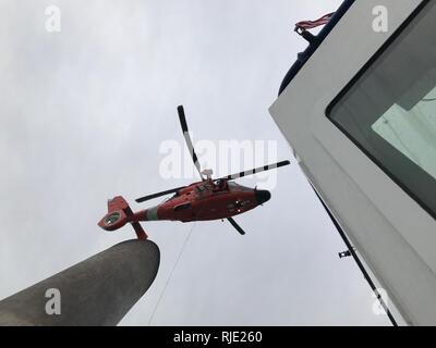 Der Küstenwache Sektor/Air Station Corpus Christi MH-65 Dolphin Hubschrauberbesatzung schwebt über dem Schiff Signet Polaris während der ersten Ausbildung evolution mit einem Signet Maritime Corporation tugboat Jan. 18, 2018, in Corpus Christi Bay. Die Ausbildung simuliert das Heben eines verletzten oder kranken Person vom Deck eines fahrenden Schiffes, auf einem Hubschrauber für den Transport auf ein höheres Niveau der medizinischen Versorgung. Stockfoto