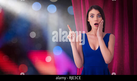Hübsche Frau vor der roten Vorhängen zeigt etwas über die theateraufführung Stockfoto