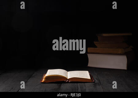 Buch der Bibel auf dunklen Tabelle öffnen. Low-key-Bild des Neuen Testaments in helles Licht bei Dunkelheit und Schatten Stockfoto