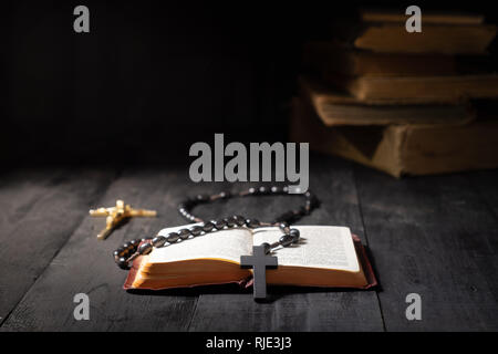 Buch der Bibel und Kruzifix auf dunklen Tabelle öffnen. Low-key-Bild des Neuen Testaments, Kreuz und Rosenkranz in helles Licht bei Dunkelheit und Schatten mit Kopieren s Stockfoto