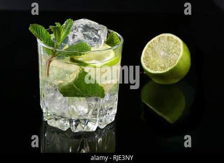 Glas Cocktail mit Rum, Kalk, Eiswürfel und Minze auf Black Mirror Hintergrund. Stockfoto