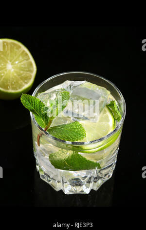 Glas Cocktail mit Rum, Kalk, Eiswürfel und Minze auf Black Mirror Hintergrund. Stockfoto