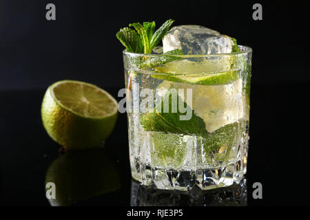 Glas Cocktail mit Rum, Kalk, Eiswürfel und Minze auf Black Mirror Hintergrund. Stockfoto