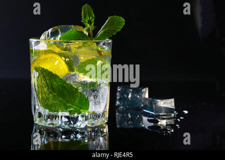 Glas Cocktail mit Rum, Kalk, Eiswürfel und Minze auf Black Mirror Hintergrund. Stockfoto