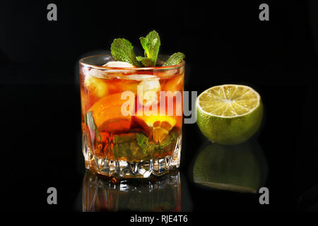 Glas dunkler Rum Cocktail mit Limone, Orange, Eiswürfel und Minze auf Black Mirror Hintergrund. Stockfoto