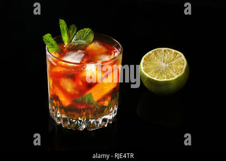Glas dunkler Rum Cocktail mit Limone, Orange, Eiswürfel und Minze auf Black Mirror Hintergrund. Stockfoto