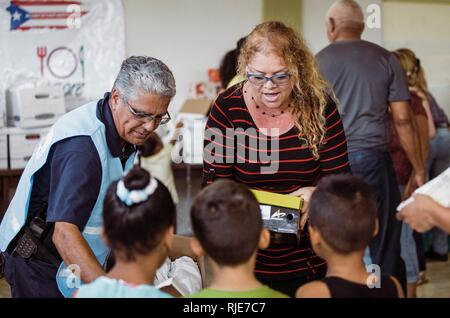 HUMACAO, Puerto Rico, 12. Januar 2018 - EIN FEMA-Mitarbeiter zusammen mit der Community Leader neue Schuhe für Kinder in Punta Santiago verteilen. Die FEMA geholfen, die Spende organisieren über 150 Paar Schuhe der Kinder auf Hurrikan Maria Überlebenden zu liefern. Eduardo Martinez/FEMA Stockfoto