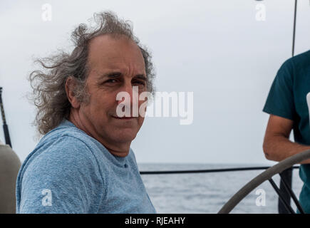 Ältere Mann sitzt auf einem Segelboot aus lächelnd die Küste von Lesbos Stockfoto