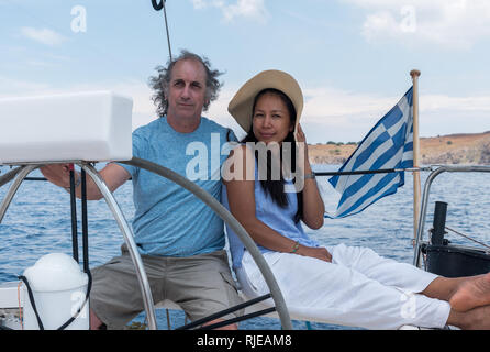 Der Mann und die Frau mit Hut im Cockpit von Segelboot mit griechischer Flagge Stockfoto