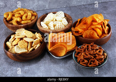 Salzige Snacks. Brezeln, Chips, Kekse in hölzernen Schüsseln. Ungesunde Produkte. Essen schlecht für Abbildung, Haut, Herz und Zähne. Sortiment von schnellen carbohydra Stockfoto