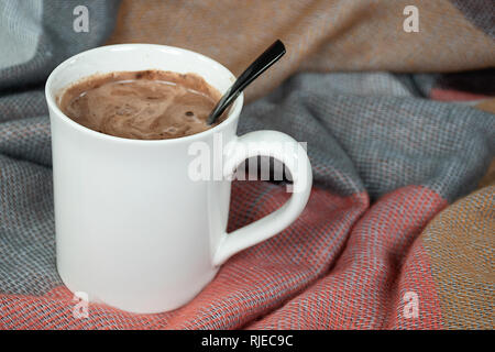 Nahaufnahme der heißen Kakao trinken in weiße Tasse mit schwarzem Löffel und weiche Decke Stockfoto