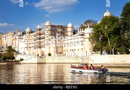 Boot mit Touristen auf dem Pichola See mit City Palace anzeigen im Blue Sky in Udaipur, Rajasthan, Indien Stockfoto