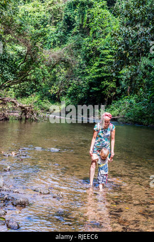 Ein schönes Foto von einer Mutter und ihrem Kind gehen Hand in Hand in einem seichten Fluss in einer wunderschönen tropischen Regenwald in Halbinsel Osa, Costa Rica Stockfoto