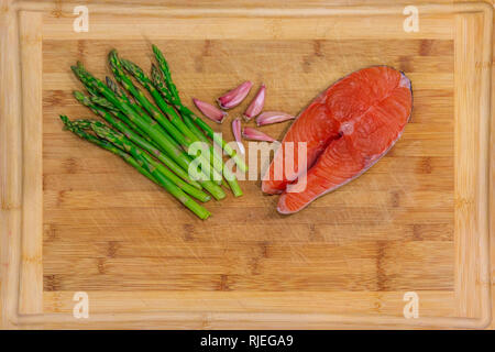 Frischer Lachs Steak mit Knoblauch und Spargel auf einer hölzernen Schneidebrett umgeben Stockfoto