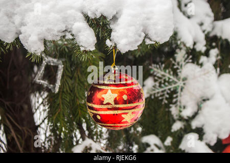 Einzelne rote weihnachtskugel mit goldglänzenden Ornamenten, die außen am echten Baum hängen Stockfoto