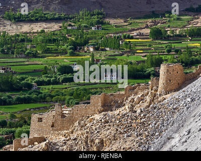 Die Ruinen einer alten tibetischen Festung vor dem hintergrund der grünen Felder und ein Dorf in einem Berg Schlucht. Stockfoto