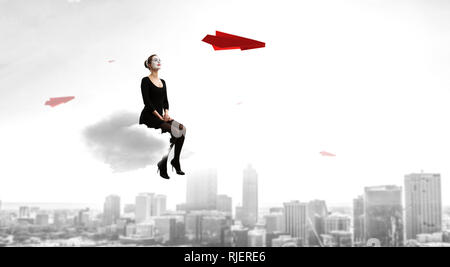 Frau mime im schwarzen Anzug sitzt auf Cloud. Mixed Media Stockfoto