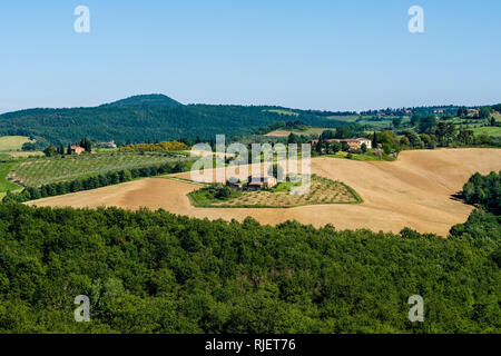 Panoramablick auf die typische hügelige toskanische Landschaft mit Feldern, Wald und einem Bauernhaus Stockfoto