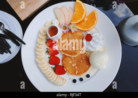 Bunte Obst Pfannkuchen mit Banane orange Erdbeeren und Ahornsirup. Stockfoto