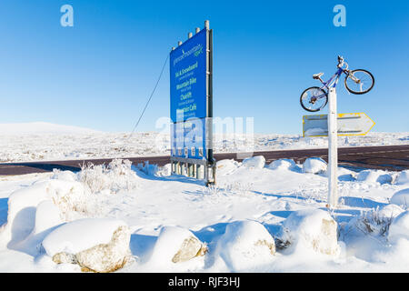 Zeichen und Mountainbike am Eingang an der A82 für das Drehen nach Glencoe Mountain Resort in Glencoe, Highlands, Schottland im Winter Stockfoto