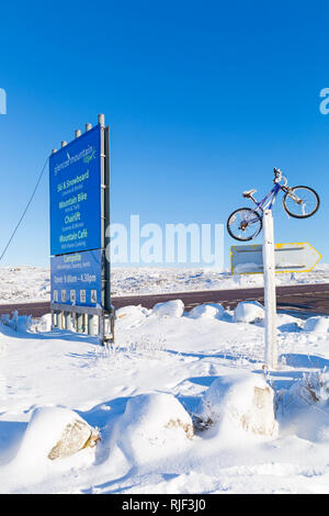 Zeichen und Mountainbike am Eingang an der A82 für das Drehen nach Glencoe Mountain Resort in Glencoe, Highlands, Schottland im Winter Stockfoto