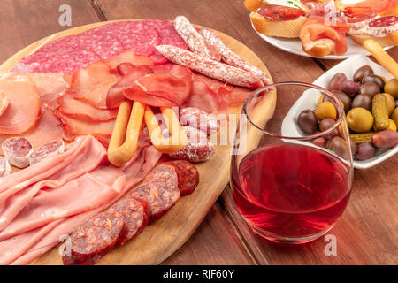 Charcuterie Verkostung. Ein Foto von vielen verschiedenen Wurst und Schinken, Aufschnitt, auf einem dunklen rustikalen Hintergrund mit einem Glas Rotwein Stockfoto