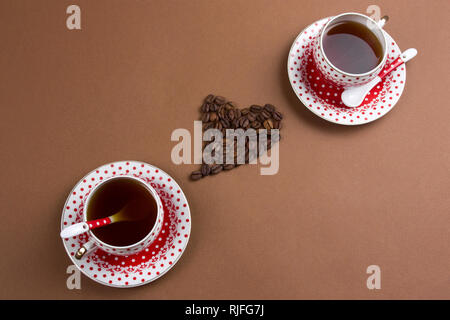 Ansicht von oben schwarz Kaffeetassen und Herzen aus Kaffeebohnen braunen Hintergrund Stockfoto