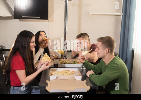 Unternehmen von vier jungen Freunde sitzen in der Küche und essen Pizza genießen. Stockfoto