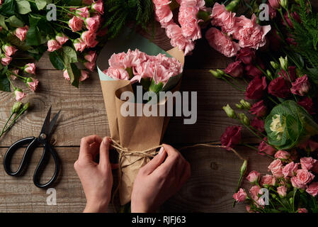 7/8 Schuß von weiblichen Händen eingabe Seil auf schönen Blumenstrauß und zarte Blumen mit Schere auf Holz- Oberfläche Stockfoto