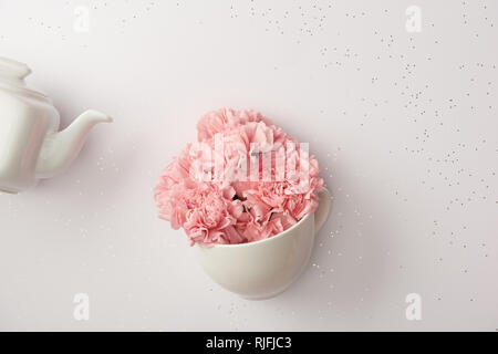 Pink carnation Blüten in Schale und Weißer Wasserkocher isoliert auf Grau Stockfoto