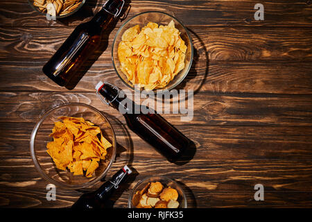 Blick von oben auf die Party Snacks in Schalen in der Nähe der braunen Flaschen mit Bier auf hölzernen Tisch Stockfoto
