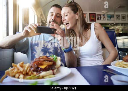 Junges Paar in Fast-Food-Restaurant unter Bild von Burger Stockfoto