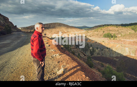 Seite Portrait von einem alten Mann mit dem weißen Haar und rot gestreifte Bluse, mit dem zaranda Minen und der Himmel bewölkt im Hintergrund, Spanien Stockfoto