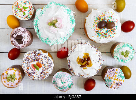 Viele verschiedene Ostern Kuchen und bunt bemalte Eier auf einem weißen Holz- Hintergrund. Ansicht von oben. Traditionelle süßes Brot dekoriert Baiser und Süßigkeiten. Stockfoto