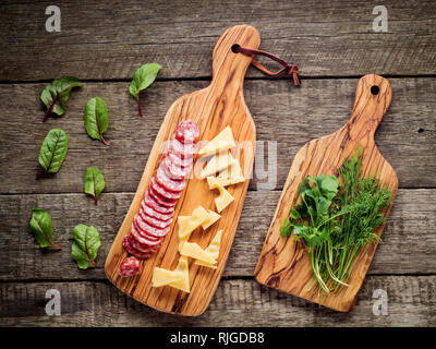 Käse und Salami auf Küche Board auf rustikalen Hintergrund. Ansicht von oben mit der Kopie Raum und Kräutern. Stockfoto