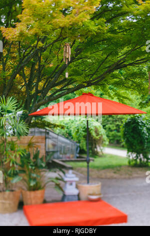 Japanisches Windspiel Holz Bambus Glocken auf Baum im Japanischen Garten mit roten Regenschirm und Töpfereien-tilt-shift Objektiv Wirkung Stockfoto