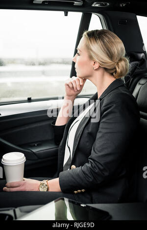 Nahaufnahme der beabsichtigten Geschäftsfrau holding Kaffee Tasse im Auto sitzen Stockfoto