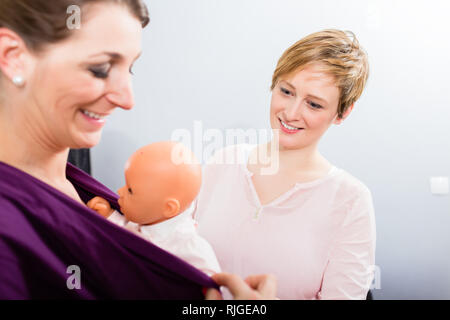 Lächelnde Ausbilder an der Frau, die dummy Baby in Schlinge suchen Stockfoto