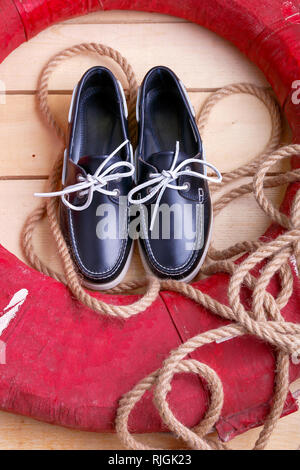 Blau Boot Schuhe auf hölzernen Hintergrund in der Nähe von Red Rettungsring und Seil. Ansicht von oben. Stockfoto