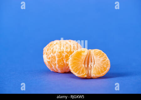 Die Hälfte der geschälten Mandarinen in der Nähe der gesamten Clementine auf blauem Hintergrund Stockfoto
