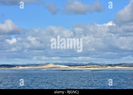 Küste mit grossen Sanddünen teilweise durch einheimische Vegetation in Northland abgedeckt und teilweise bewölkt aber ansonsten blauen Himmel über Öffnen. Stockfoto