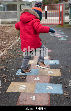 Junge spielt Hopse im Park im roten Mantel, Mütze und Handschuhe mit Kugelelementen Stockfoto