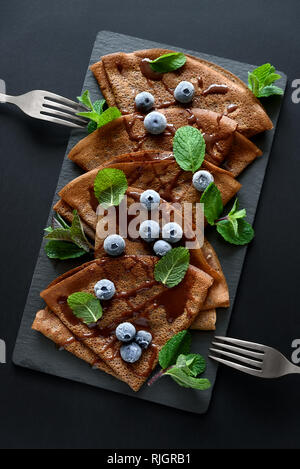 Hausgemachte Schokolade Pfannkuchen mit Heidelbeeren, Soße und Minze auf schiefer Teller serviert. Selektive konzentrieren. Ansicht von oben. Platz kopieren Stockfoto