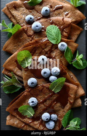 Hausgemachte Schokolade Pfannkuchen mit Heidelbeeren, Soße und Minze auf schiefer Teller serviert. Selektive konzentrieren. Ansicht von oben. Platz kopieren Stockfoto