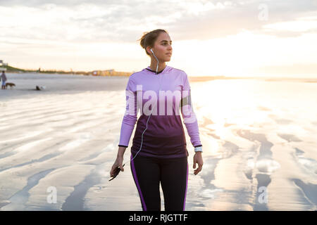 Läuferin erholt, nachdem sie auf einem Strand bei Sonnenaufgang Stockfoto