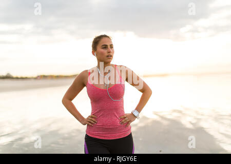 Läuferin erholt, nachdem sie auf einem Strand bei Sonnenaufgang Stockfoto