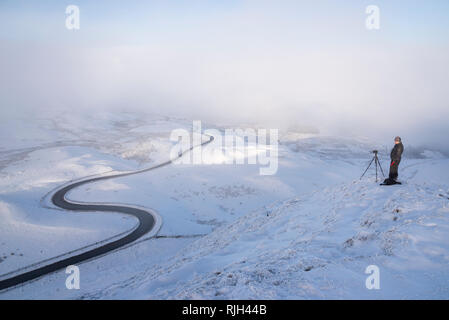 Fotograf auf Mam Tor im Peak District National Park. Die berühmte bendy Straße, die zur edale an einem verschneiten Wintermorgen. Stockfoto