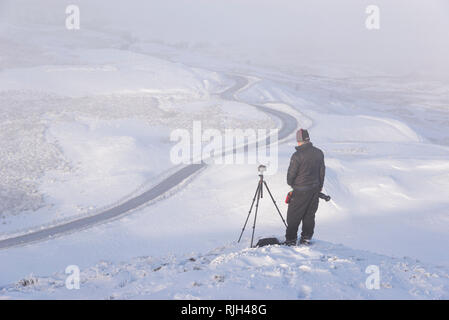 Fotograf auf Mam Tor im Peak District National Park. Die berühmte bendy Straße, die zur edale an einem verschneiten Wintermorgen. Stockfoto